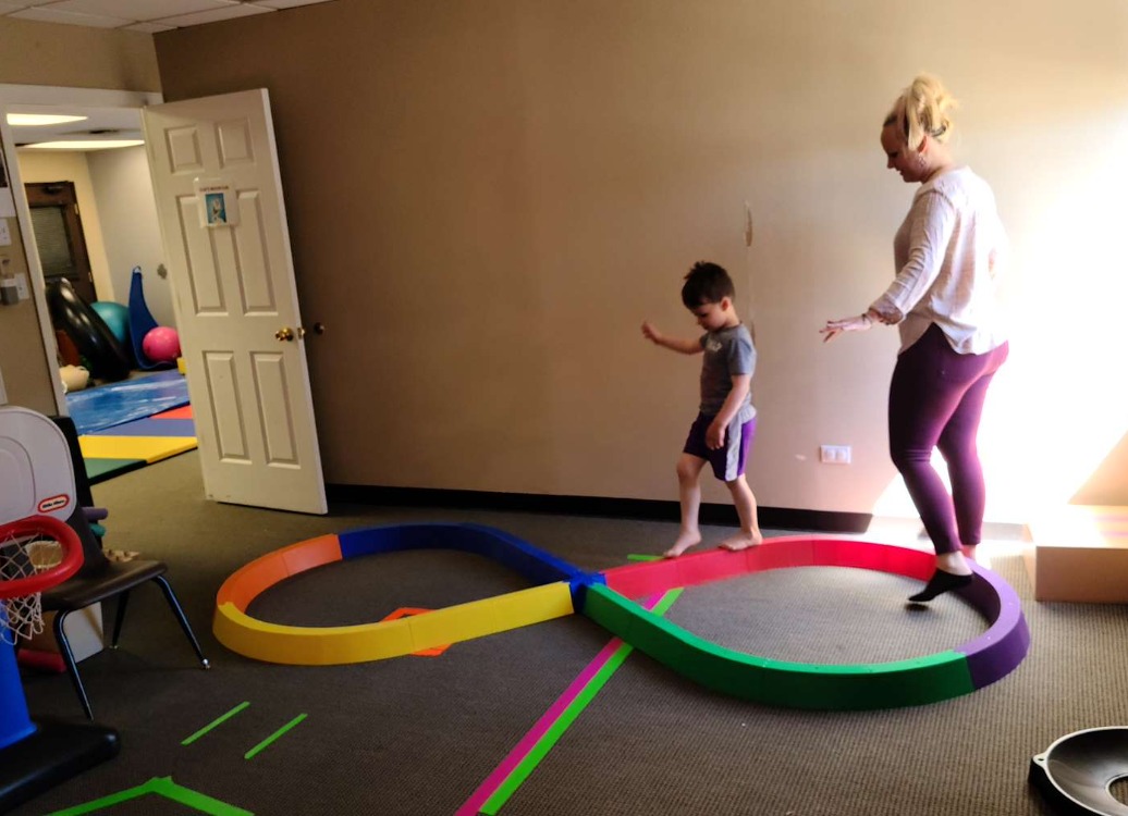 A child walking a colorful foam balance path with a therapist alongside