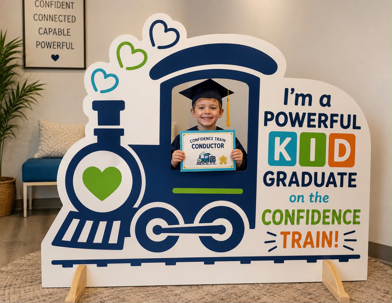 A child holding a Confidence Train conductor certificate beside the Powerful Kids Therapy sign